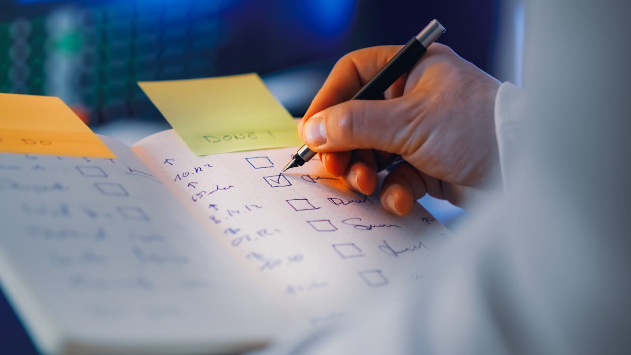 Close-up of a hand writing in a notebook with checkboxes, highlighting productivity and organization.